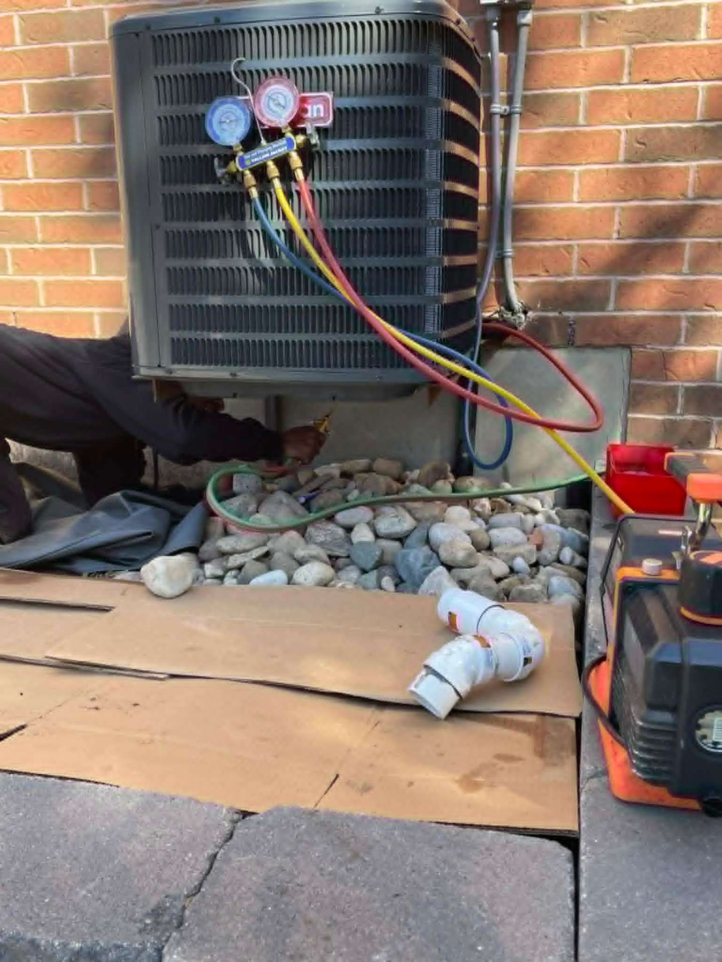 Draco technician evacuating and charging an outdoor AC condenser with manifold gauges